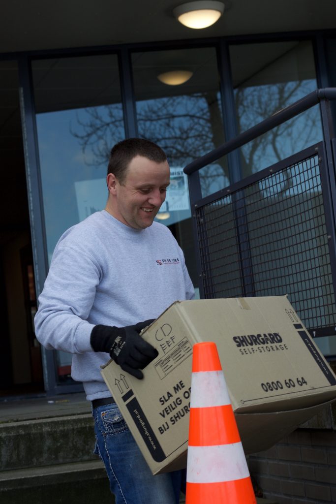 SW de Vries Verhuizingen tilt een doos naar buiten.