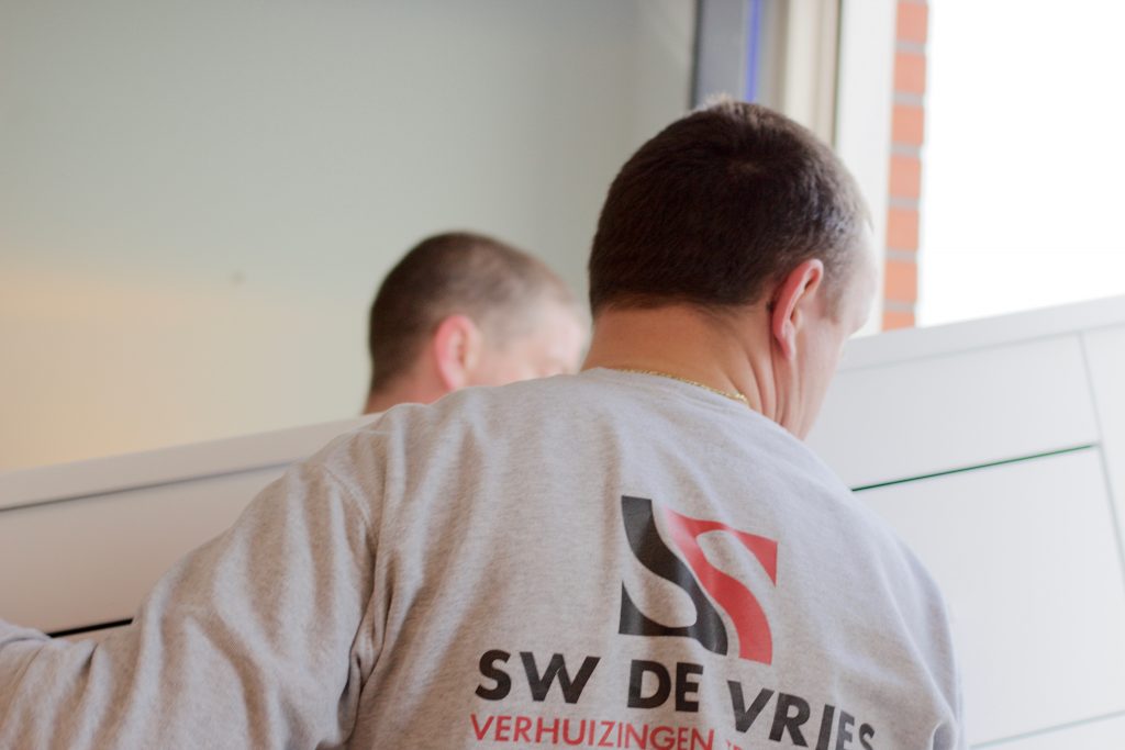 Twee mannen van SW de Vries Verhuizingen tillen een kast door het raam naar buiten