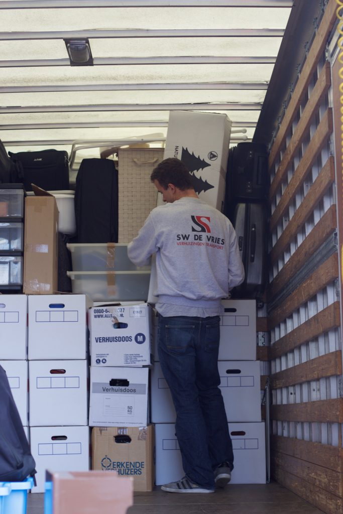 SW de Vries zet een doos met een kerstboom in een verhuisbus.